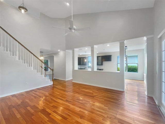 unfurnished living room featuring baseboards, a towering ceiling, stairway, wood finished floors, and ornate columns