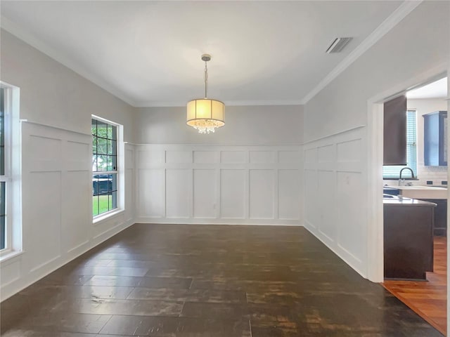 unfurnished dining area featuring visible vents, dark wood-style floors, ornamental molding, a decorative wall, and a sink