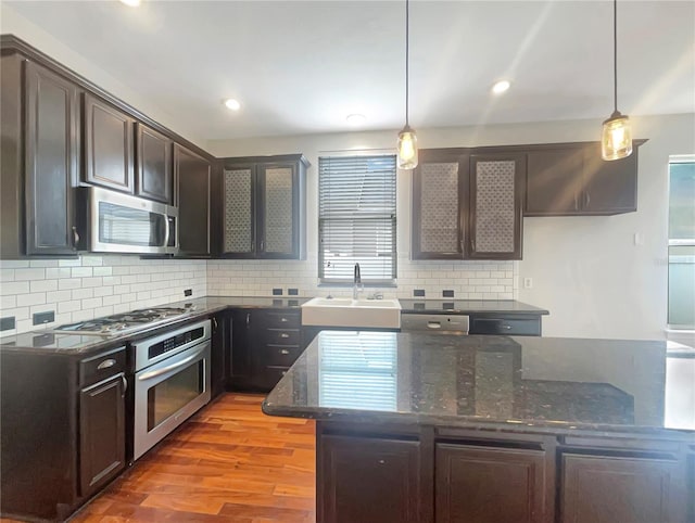 kitchen featuring stainless steel appliances, light hardwood / wood-style flooring, tasteful backsplash, sink, and dark stone countertops