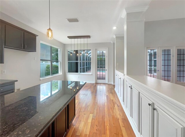 kitchen with pendant lighting, light wood finished floors, visible vents, dark brown cabinetry, and dark stone countertops