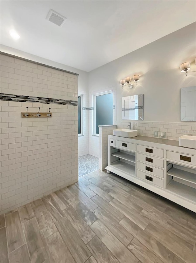 bathroom with double vanity, visible vents, wood finished floors, walk in shower, and a sink