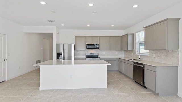 kitchen with sink, gray cabinets, backsplash, stainless steel appliances, and a center island