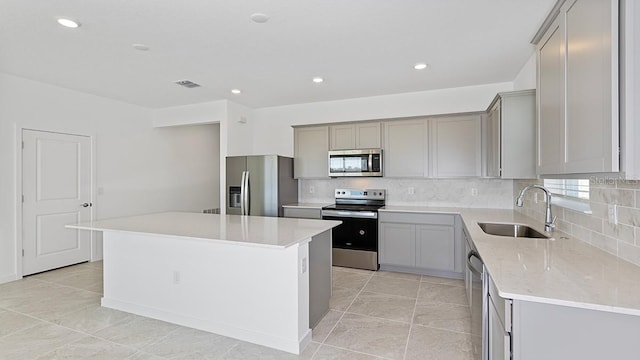 kitchen featuring sink, a center island, appliances with stainless steel finishes, gray cabinets, and backsplash