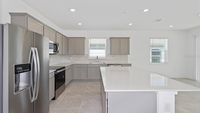 kitchen featuring a kitchen island, appliances with stainless steel finishes, sink, backsplash, and light stone counters