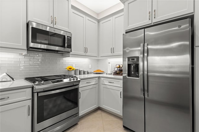 kitchen with appliances with stainless steel finishes, white cabinets, light tile patterned floors, and tasteful backsplash