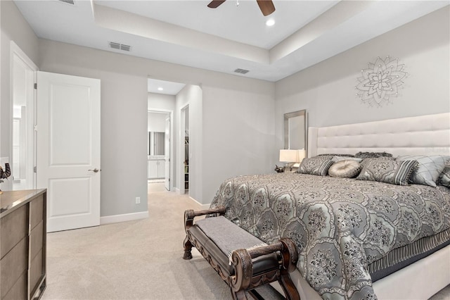 bedroom featuring ceiling fan, light carpet, a raised ceiling, and connected bathroom