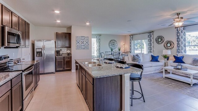 kitchen with ceiling fan, a center island with sink, light tile patterned floors, and stainless steel appliances