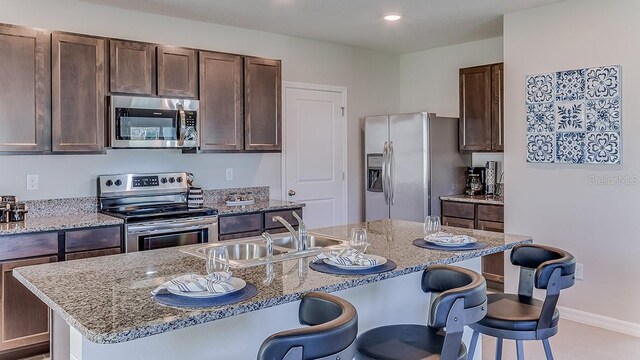 kitchen featuring a kitchen island with sink, appliances with stainless steel finishes, sink, and light stone counters