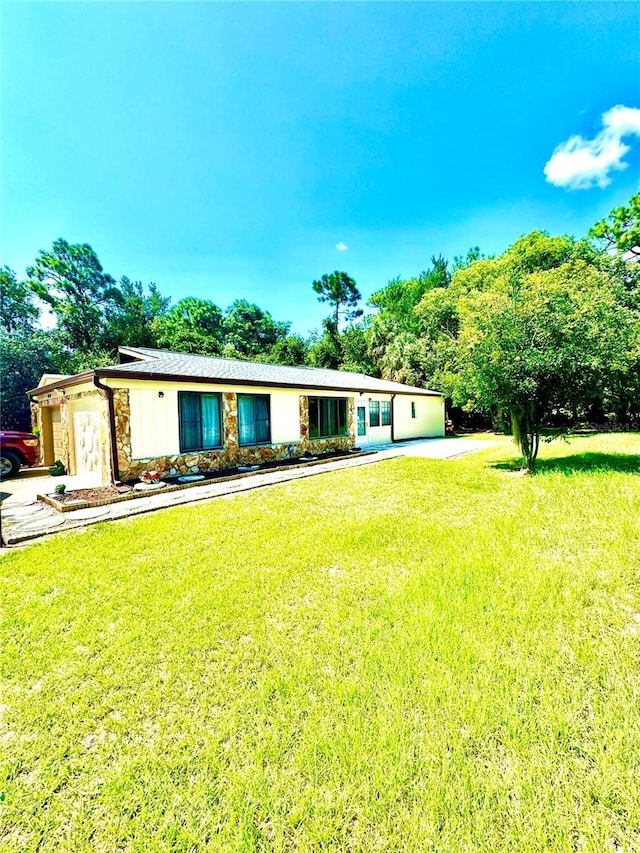 view of front of house with an attached garage, stone siding, and a front yard