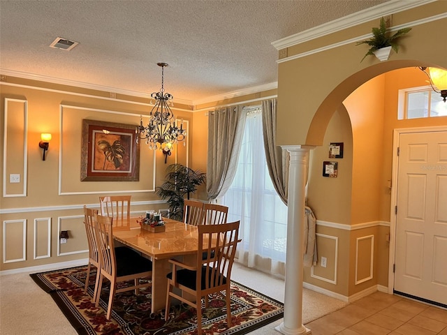 dining area featuring crown molding, an inviting chandelier, a textured ceiling, light tile patterned floors, and ornate columns