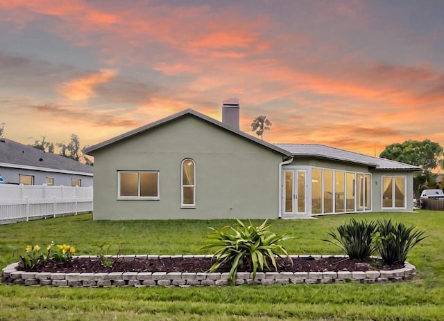 back of house at dusk featuring french doors, a yard, stucco siding, and fence
