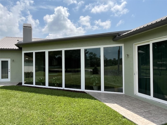back of property featuring a yard, stucco siding, and a chimney