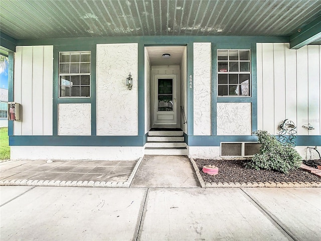 entrance to property with stucco siding, covered porch, and board and batten siding