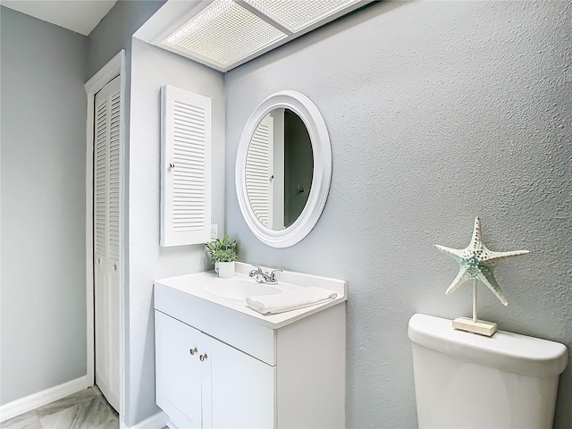 bathroom featuring baseboards, toilet, a textured wall, a closet, and vanity