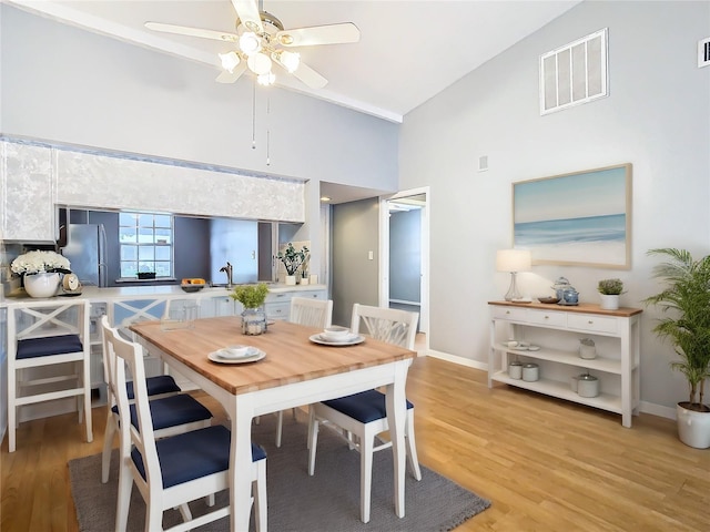 dining area with a ceiling fan, baseboards, visible vents, high vaulted ceiling, and light wood-style floors