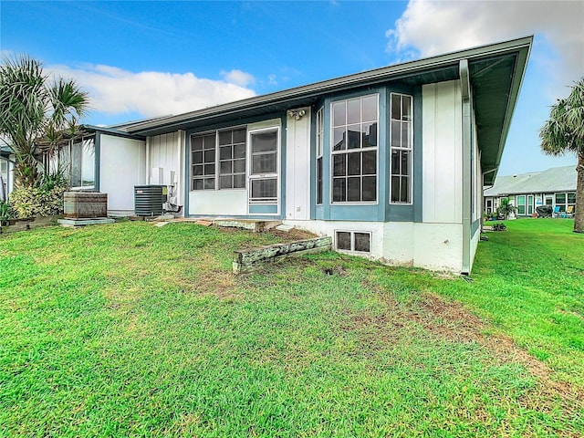 rear view of property with board and batten siding, a lawn, and central AC