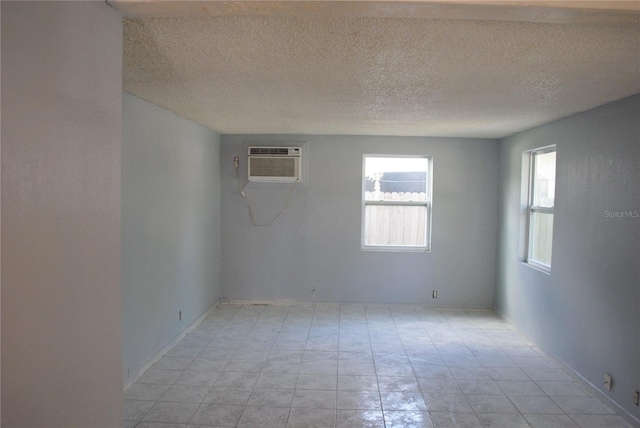 empty room with light tile patterned floors, a wall mounted air conditioner, and a textured ceiling