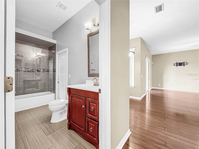 full bathroom with vanity, bath / shower combo with glass door, hardwood / wood-style floors, and toilet