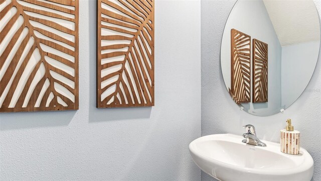 bathroom featuring lofted ceiling, a textured wall, and a sink