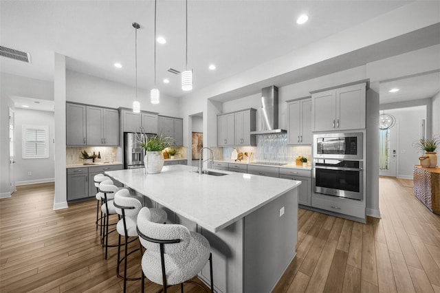 kitchen featuring visible vents, gray cabinets, a sink, appliances with stainless steel finishes, and wall chimney exhaust hood