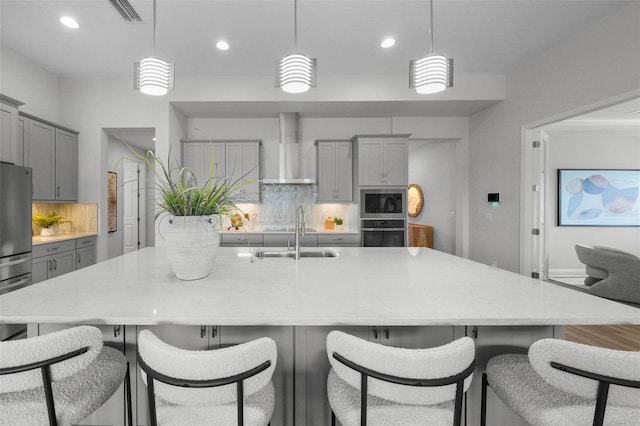 kitchen featuring visible vents, gray cabinetry, a sink, stainless steel appliances, and wall chimney exhaust hood