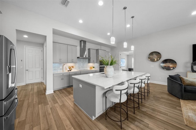 kitchen with visible vents, gray cabinetry, wall chimney exhaust hood, stainless steel fridge with ice dispenser, and light wood finished floors