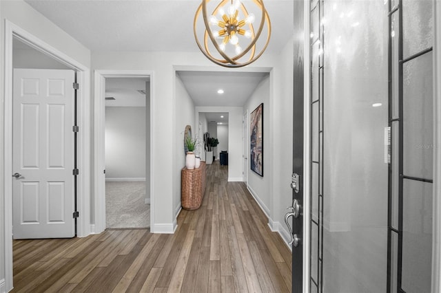 corridor with baseboards, an inviting chandelier, and wood finished floors