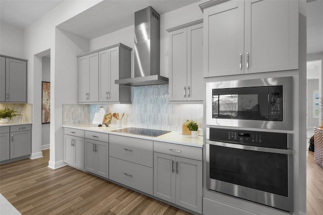 kitchen featuring stainless steel appliances, gray cabinetry, light wood-style flooring, and wall chimney range hood