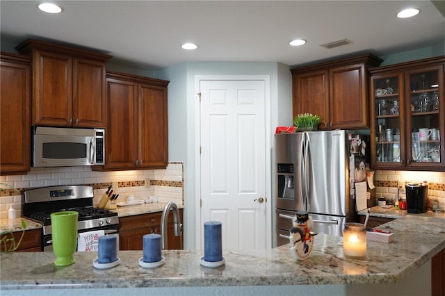 kitchen with tasteful backsplash, sink, light stone countertops, appliances with stainless steel finishes, and kitchen peninsula