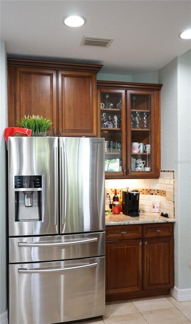 kitchen featuring light stone counters, light tile patterned floors, tasteful backsplash, and stainless steel fridge with ice dispenser