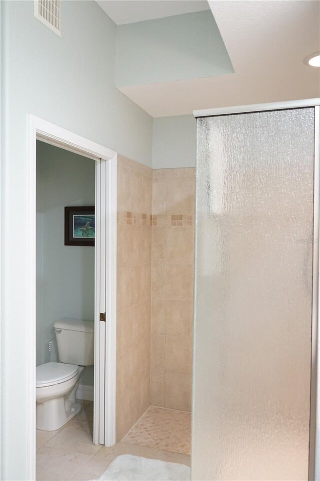 bathroom featuring a tile shower, tile patterned flooring, and toilet