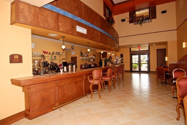 bar featuring a high ceiling, pendant lighting, french doors, and light tile patterned floors