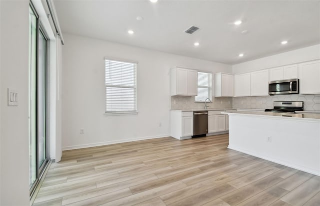 kitchen featuring white cabinetry, light wood-type flooring, stainless steel appliances, and tasteful backsplash