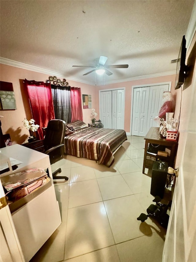 bedroom with a textured ceiling, tile patterned flooring, ornamental molding, two closets, and ceiling fan