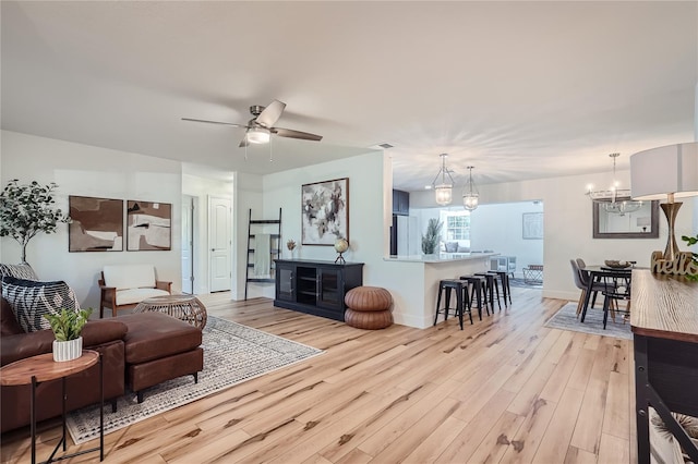 living room with ceiling fan with notable chandelier and light wood-type flooring