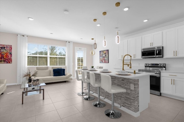 kitchen with white cabinetry, decorative light fixtures, light tile patterned floors, stainless steel appliances, and a kitchen island with sink