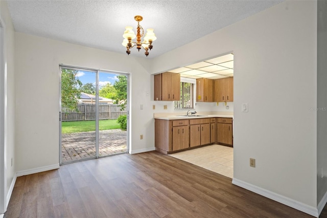 kitchen with sink, a notable chandelier, pendant lighting, a textured ceiling, and light wood-type flooring