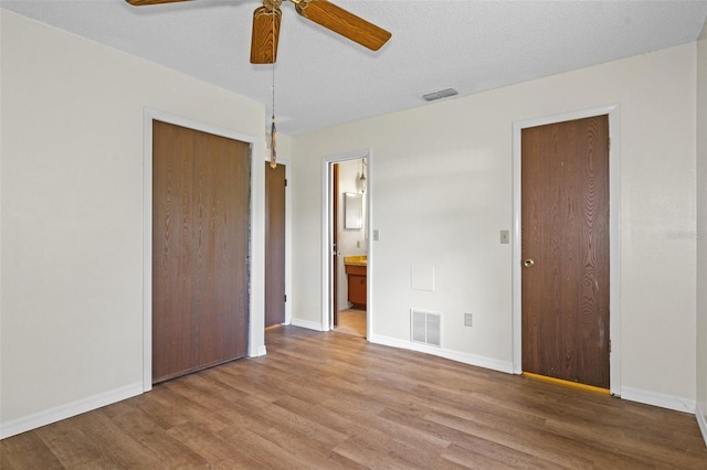 unfurnished bedroom with a textured ceiling, ceiling fan, hardwood / wood-style flooring, connected bathroom, and a closet