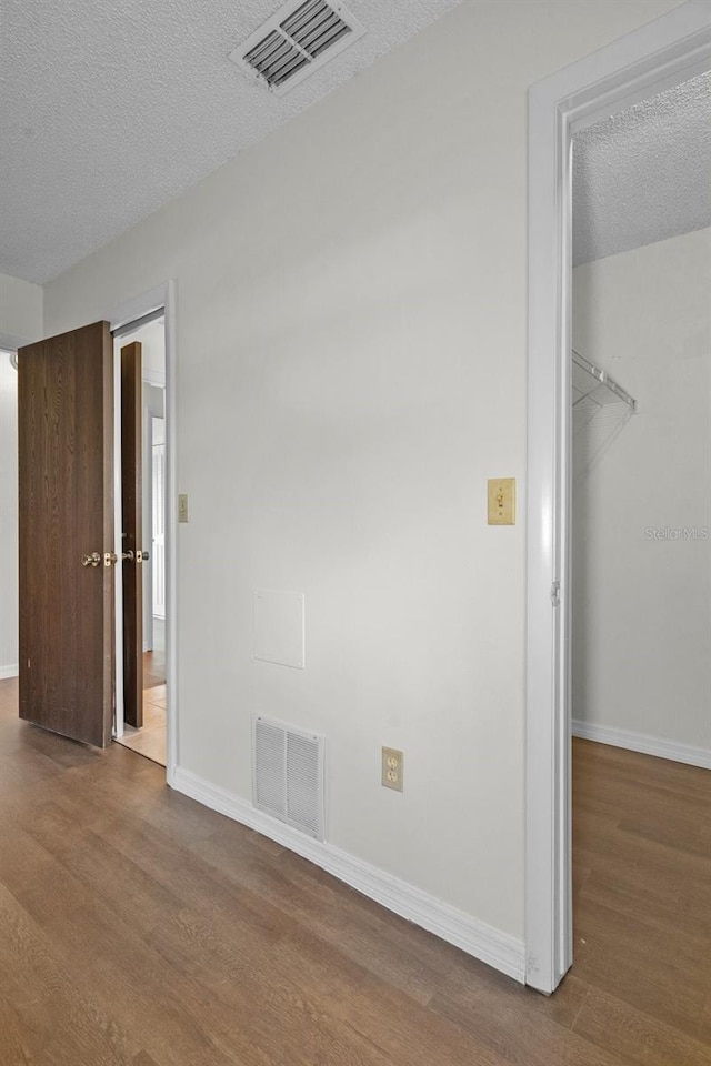 unfurnished bedroom featuring hardwood / wood-style flooring, a walk in closet, a textured ceiling, and a closet