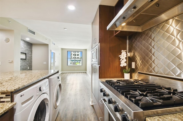 kitchen with light stone countertops, wall chimney exhaust hood, light hardwood / wood-style floors, tasteful backsplash, and high end range