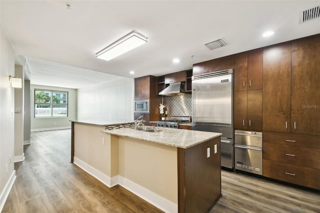 kitchen featuring an island with sink, light hardwood / wood-style flooring, built in appliances, and backsplash