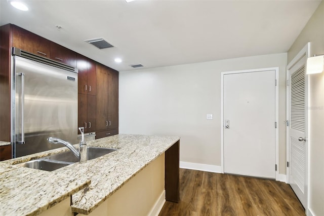 kitchen featuring built in fridge, light stone countertops, dark hardwood / wood-style floors, and sink