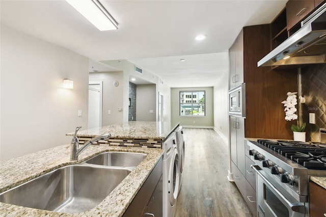 kitchen with hardwood / wood-style floors, stainless steel appliances, exhaust hood, light stone counters, and sink