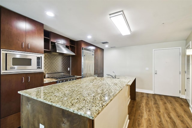 kitchen with built in appliances, hardwood / wood-style floors, and a center island with sink