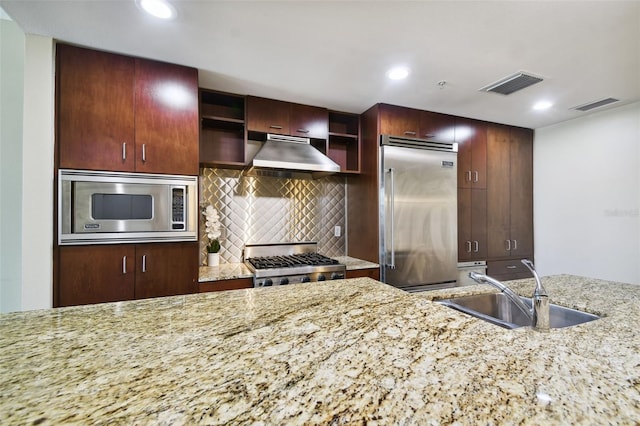 kitchen featuring built in appliances, light stone countertops, range hood, tasteful backsplash, and sink