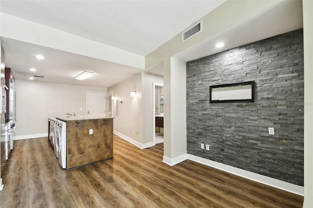 kitchen featuring washer / clothes dryer, dark hardwood / wood-style floors, light stone countertops, and a kitchen island with sink