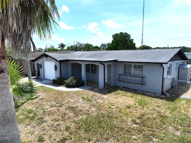 ranch-style home featuring a garage, a shingled roof, stucco siding, fence, and a front yard