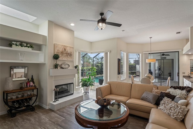 living room with ceiling fan, dark hardwood / wood-style floors, a textured ceiling, and a fireplace