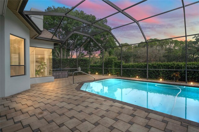 pool at dusk featuring glass enclosure and a patio