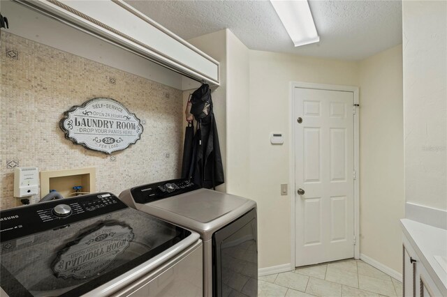 washroom featuring light tile patterned flooring, washing machine and clothes dryer, a textured ceiling, and cabinets